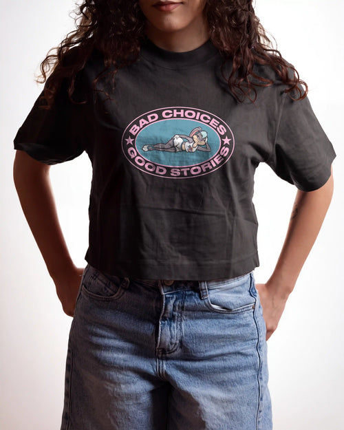 woman wearing an off black crop top t-shirt with a bad choices good stories graphic printed on it on a white background