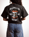 A person shown from the back wearing a black graphic T-shirt and blue jeans against a plain light background. The shirt features a large apple-and-skull design with the text 'AN APPLE A DAY YOU DIE ANYWAY'.