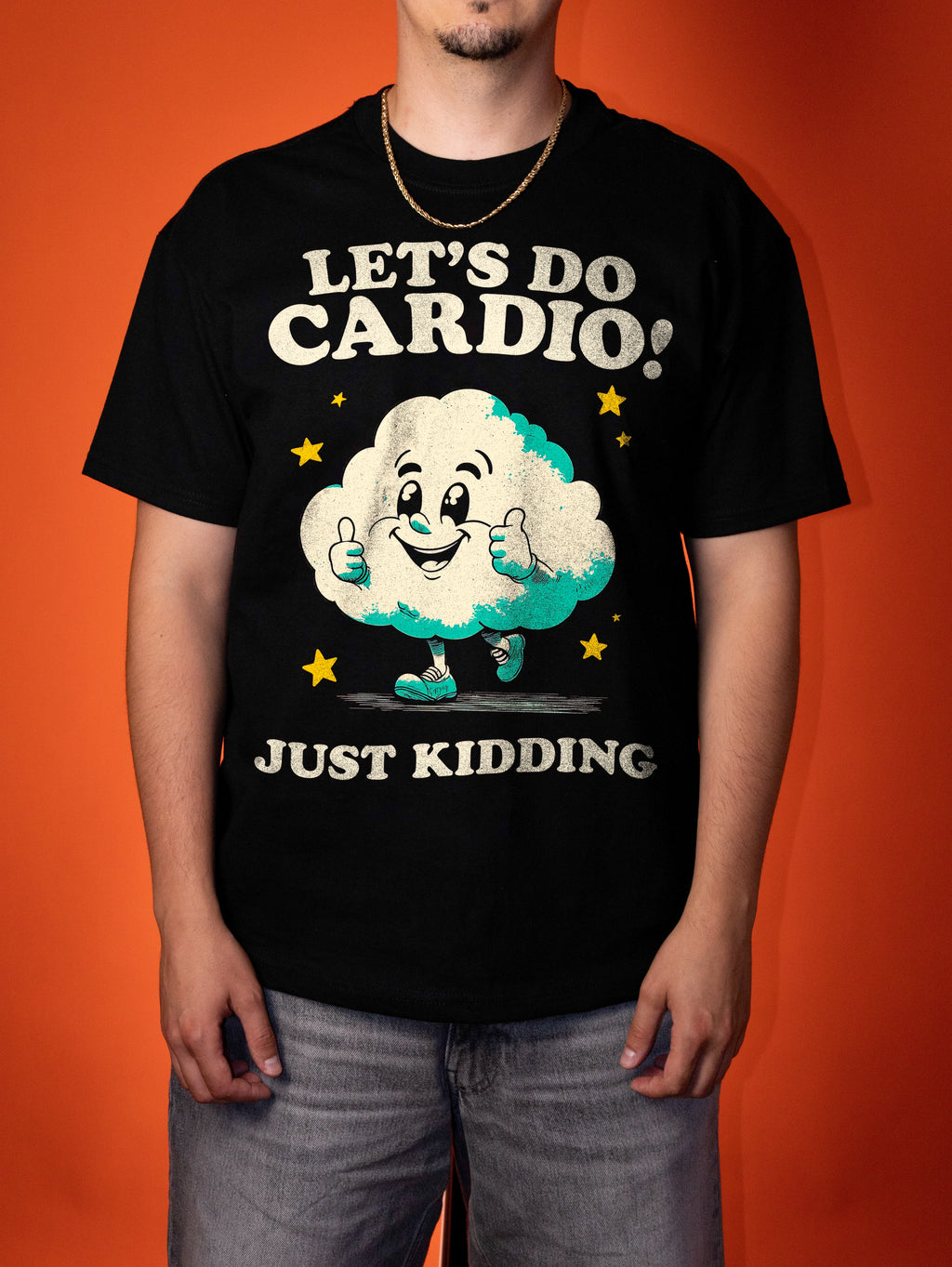 A man wearing a black graphic t-shirt with a cartoon cloud character and the text 'LET'S DO CARDIO! JUST KIDDING' against an orange background.