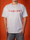 A man wearing a white short-sleeve t-shirt with 'DADLIFT' printed in red across the chest, paired with gray jeans and a gold chain necklace, set against a solid orange background.