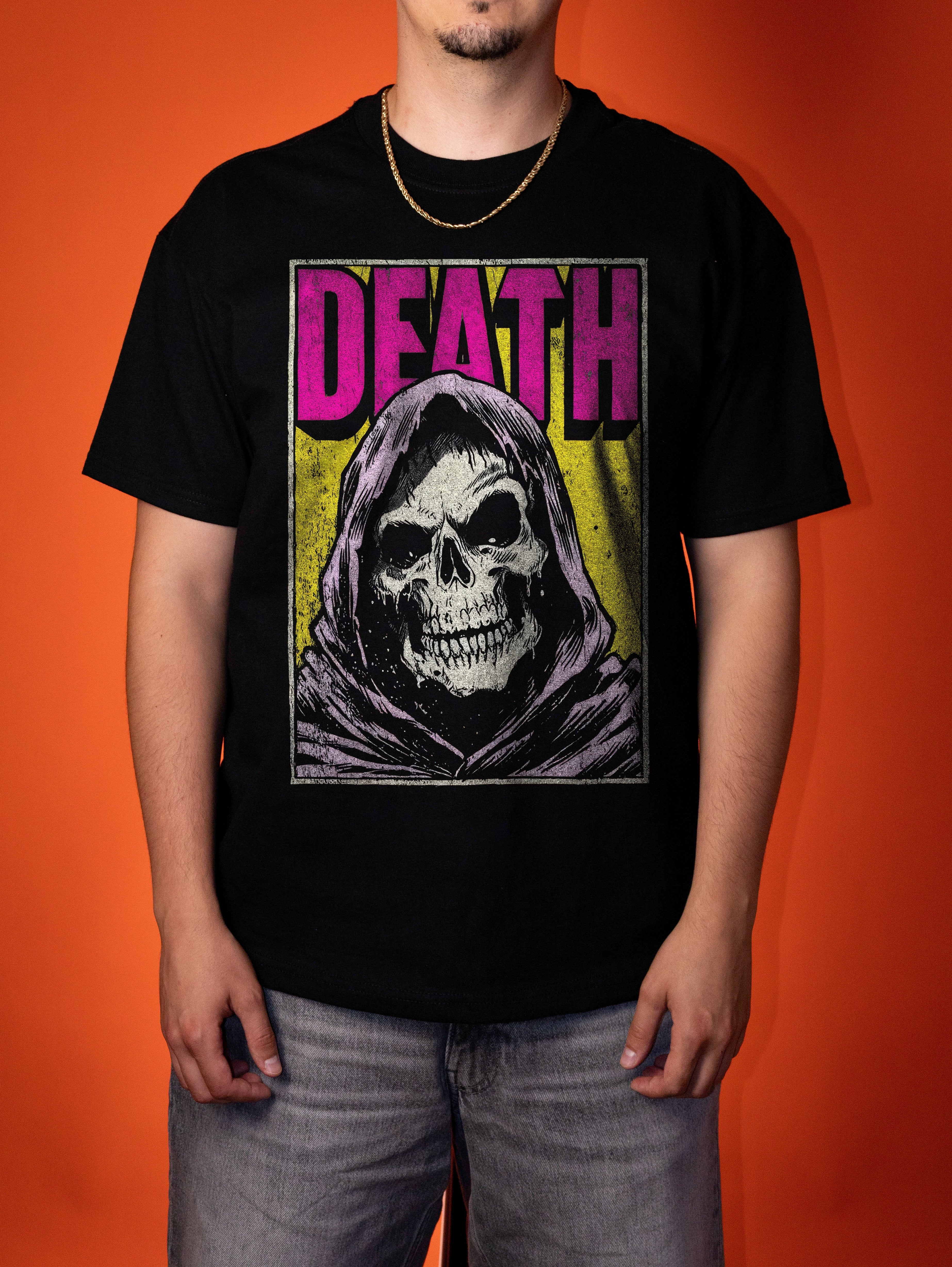 A man wearing a black graphic t-shirt featuring a grim reaper design with the word 'DEATH' in pink, set against a solid orange background.