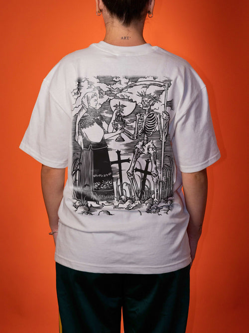 A person viewed from the back wearing a white oversized T-shirt with a large black illustrated graphic across the back, paired with dark pants, against a solid orange background.