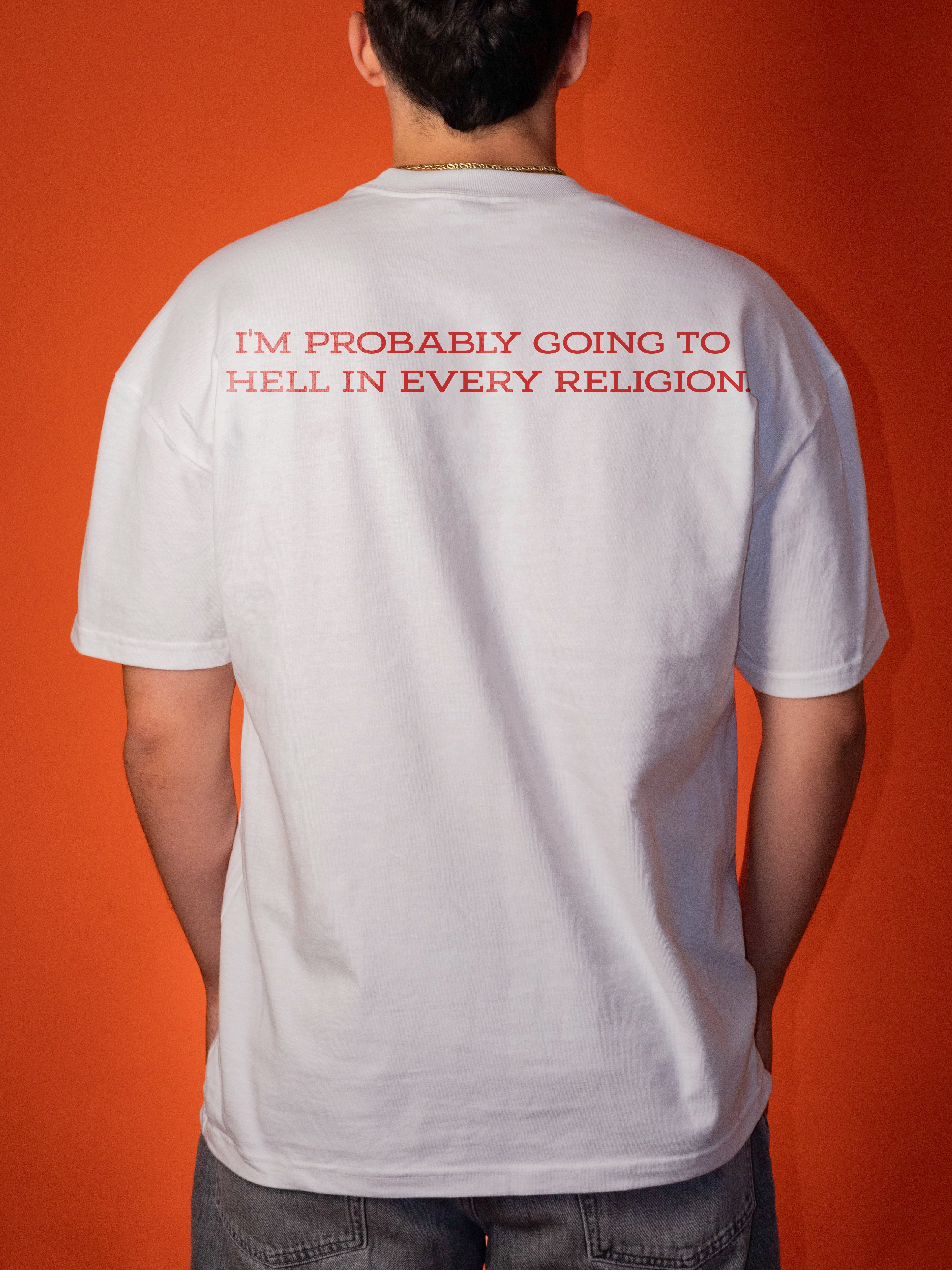 A man viewed from behind wearing a white t-shirt with red text that reads 'I'M PROBABLY GOING TO HELL IN EVERY RELIGION' against a solid orange background.