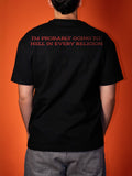 A person viewed from behind wearing a black short-sleeve T-shirt with red text on the upper back that reads, 'I'M PROBABLY GOING TO HELL IN EVERY RELIGION.' against a solid orange background.