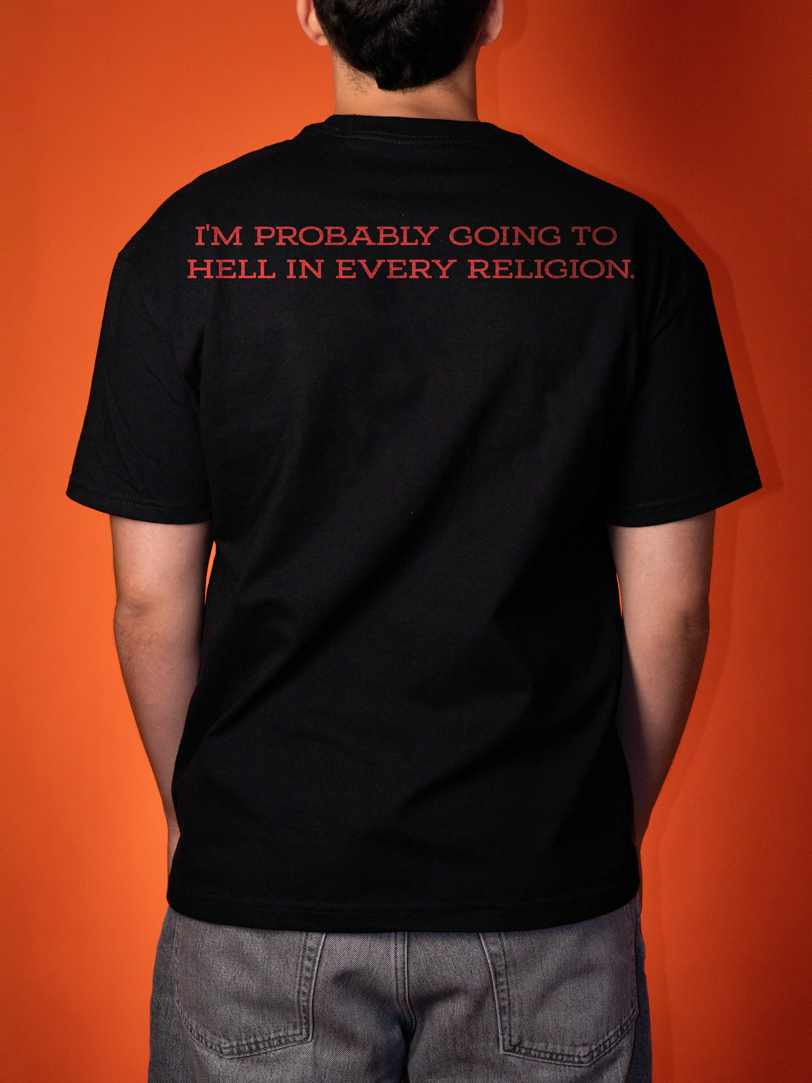 A person viewed from behind wearing a black short-sleeve T-shirt with red text on the upper back that reads, 'I'M PROBABLY GOING TO HELL IN EVERY RELIGION.' against a solid orange background.