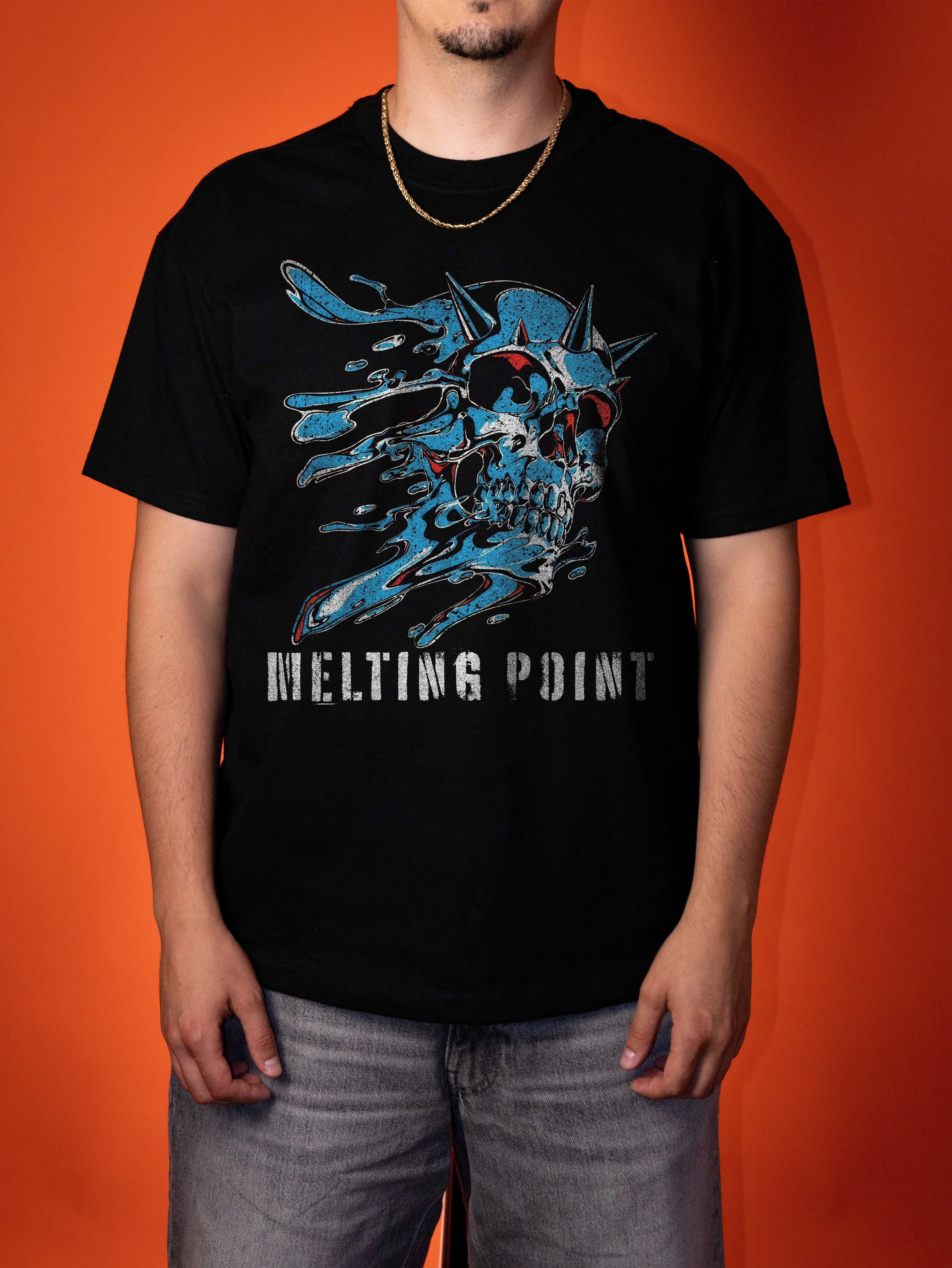 A man wearing a black short-sleeve t-shirt with a blue melting skull graphic and the text 'MELTING POINT' on the front, paired with gray jeans, set against a solid orange background.