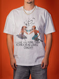 A man wearing a white graphic t-shirt with a cartoon illustration of two skeletons and the text 'I LOVE YOU MORE THAN A CRACK HEAD LOVES CRACK!!!' against a solid orange background.