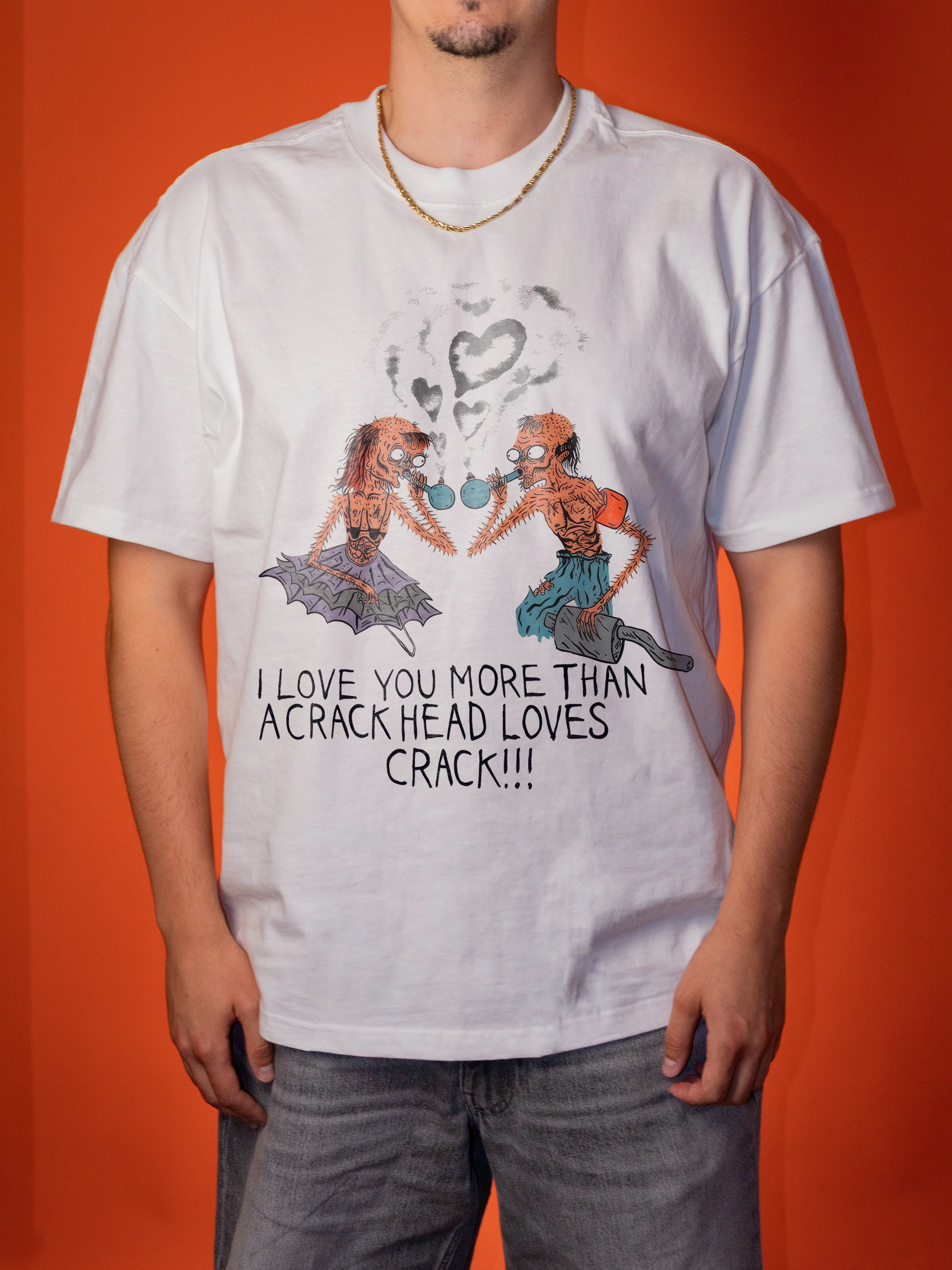 A man wearing a white graphic t-shirt with a cartoon illustration of two skeletons and the text 'I LOVE YOU MORE THAN A CRACK HEAD LOVES CRACK!!!' against a solid orange background.