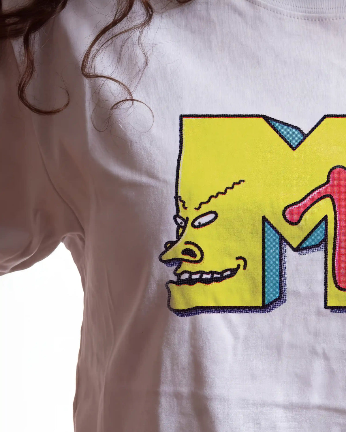 A close-up of a white short-sleeve t-shirt featuring a large graphic print of a yellow cartoon monster face inside a bold yellow letter 'M' with blue and red accents.