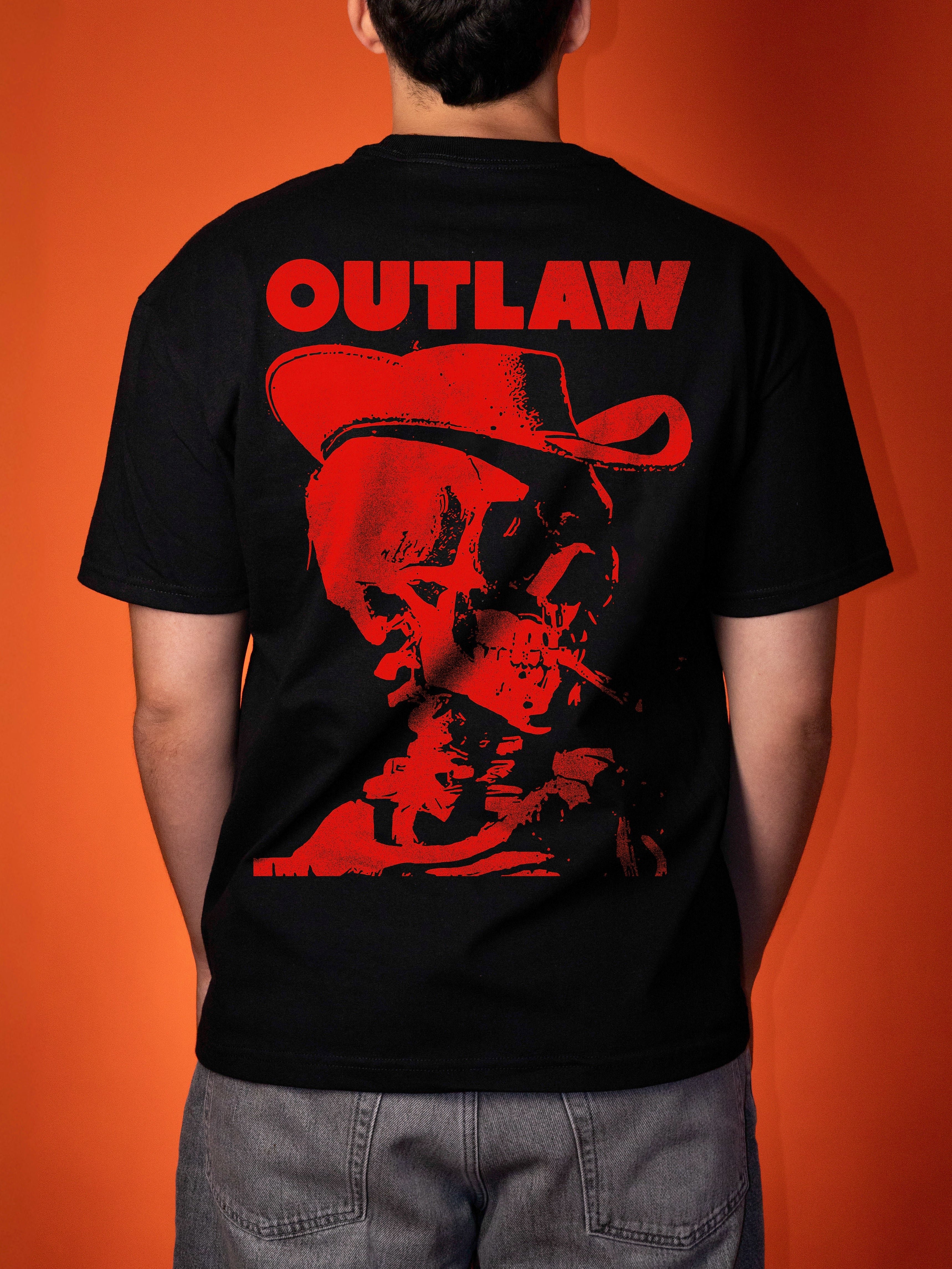 A person viewed from the back wearing a black short-sleeve T-shirt with a large red graphic print on the back featuring the word 'OUTLAW' above a red cowboy hat and skull illustration, against an orange background.