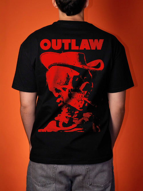 A person viewed from the back wearing a black short-sleeve T-shirt with a large red graphic print on the back featuring the word 'OUTLAW' above a red cowboy hat and skull illustration, against an orange background.