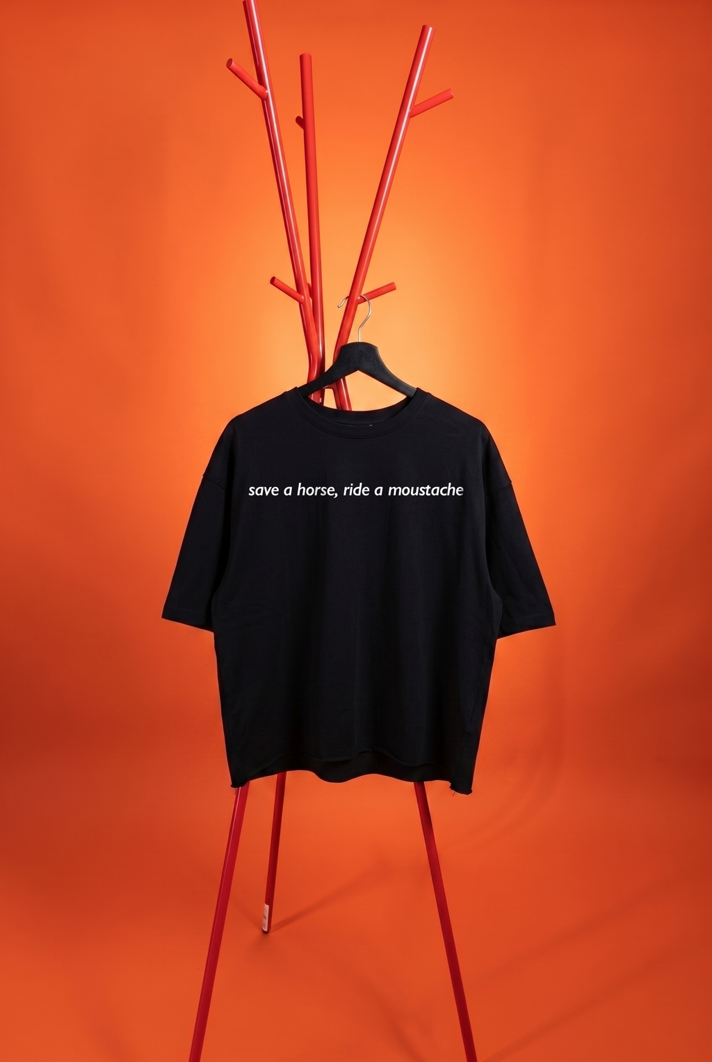 Black t-shirt with text 'save a horse, ride a moustache' on a hanger against an orange background