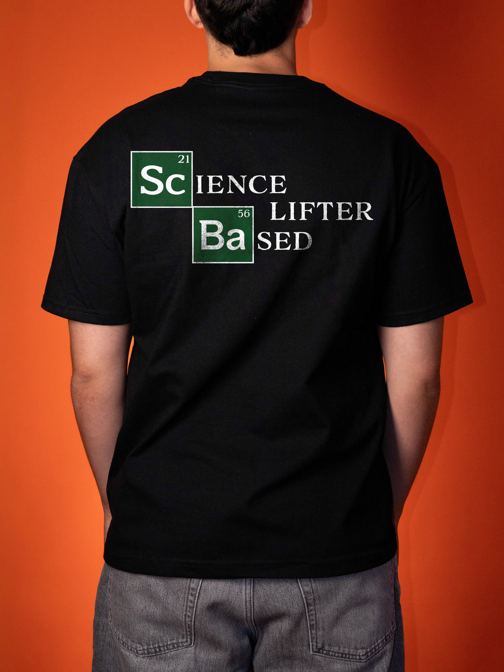 A person viewed from the back wearing a black t-shirt with a 'Science Lifter sed' graphic printed on the back, set against a solid orange background.