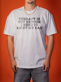 A man wearing a white graphic t-shirt with the text 'THERAPY IS NOT ENOUGH I NEED TO FIGHT MY DAD' printed in black distressed lettering, set against a solid orange background.
